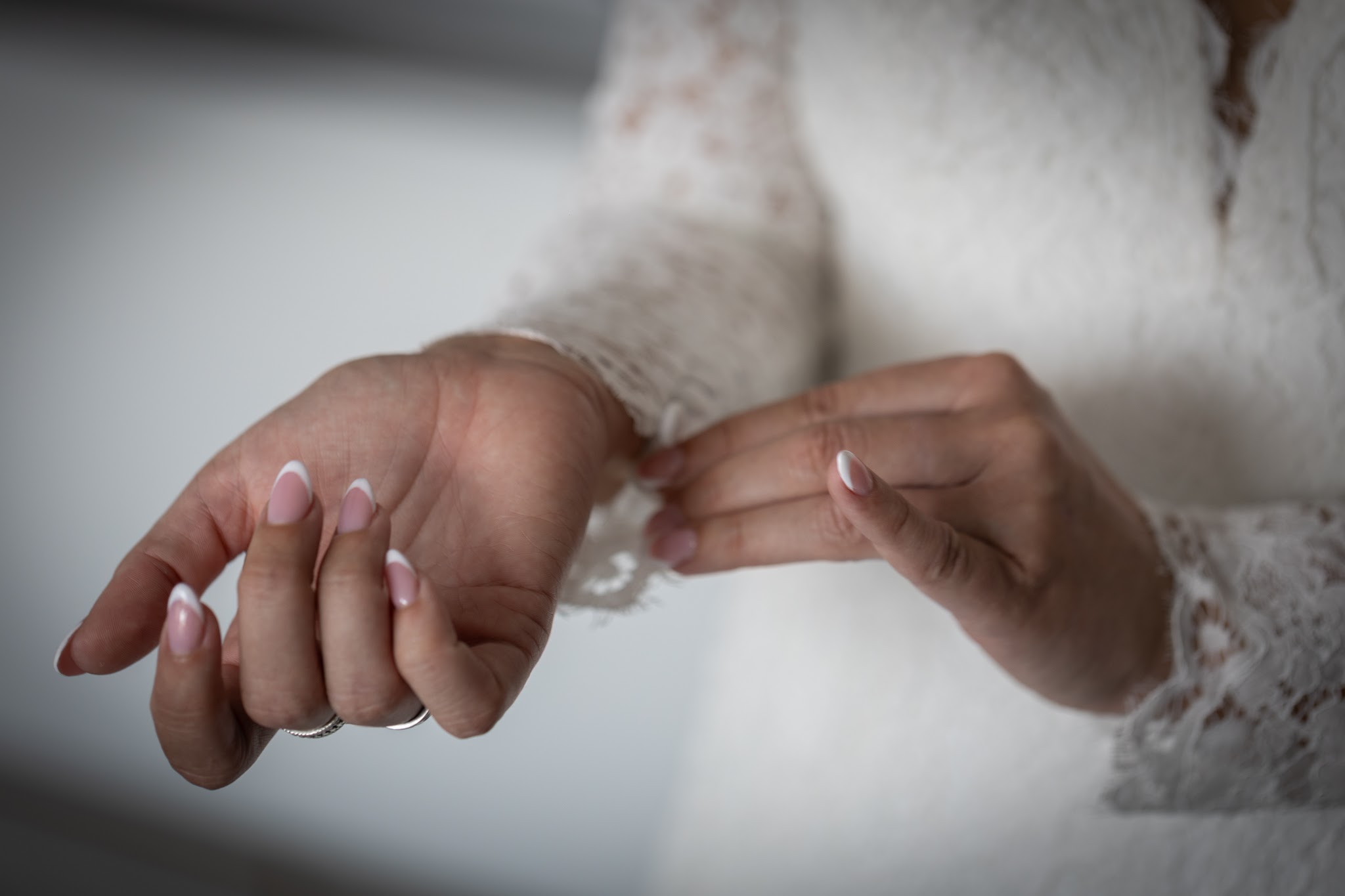 Handen van een bruid met naturel French nagels en een kanten mouw
